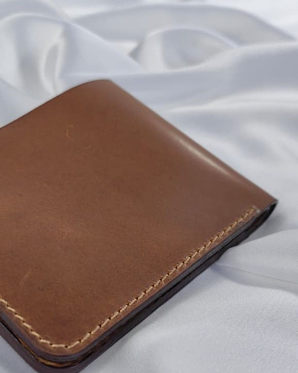 Full-grain leather bifold wallet, closed, on white satin