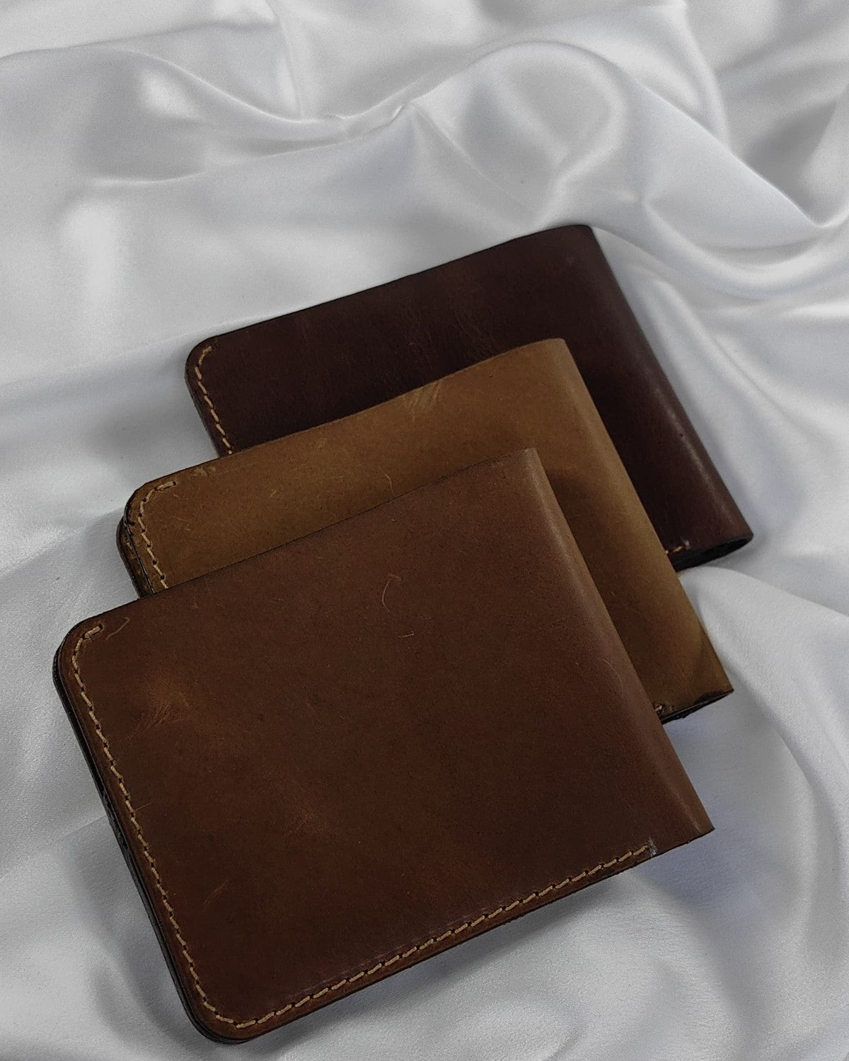 Three full-grain leather bifold wallets in different leather shades